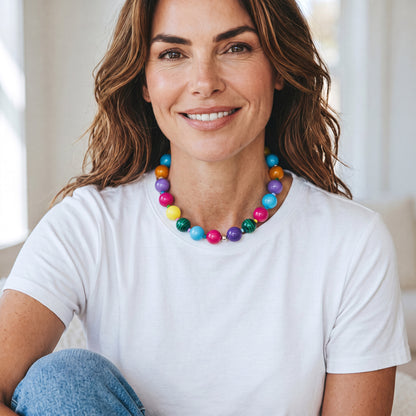 A woman wearing a Robyn by design multi-colored beaded statement necklace with glossy spherical beads in vibrant hues.